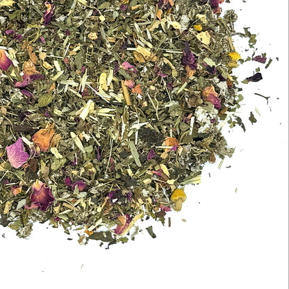 A close-up of dried loose leaf tea blend, including herbs such as raspberry leaf, nettle, ginger, oatstraw, rose petals, lemon balm, and chamomile, with the brand logo 'GRASSROOTS HERB SUPPLY' visible.